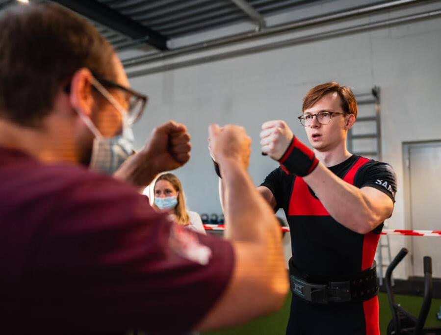 Powerlifting coach Julian Kohler fist bumping athlete after achieving a personal record at a competition in Switzerland, capturing peak performance, strength progress, and coaching success.