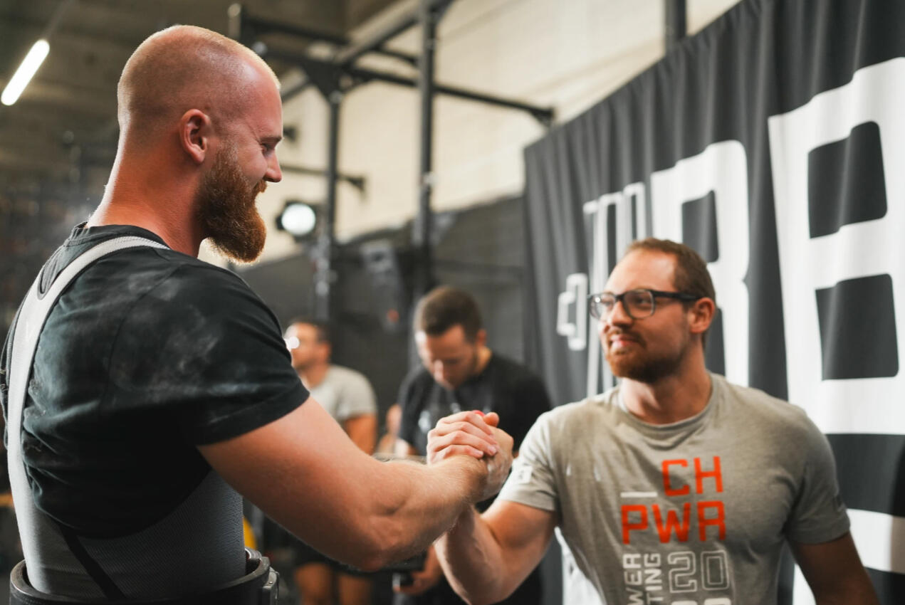 Powerlifting coach and athlete shaking hands after a successful lift, symbolizing trust, progress, and results in strength training and competitive powerlifting.